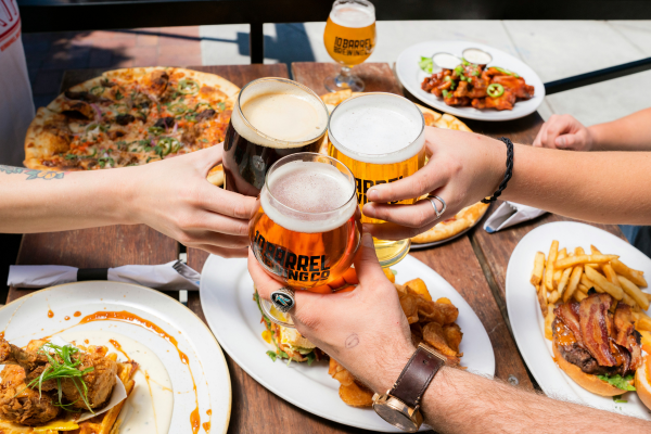 three people toasting with glasses of beer over a table of food
