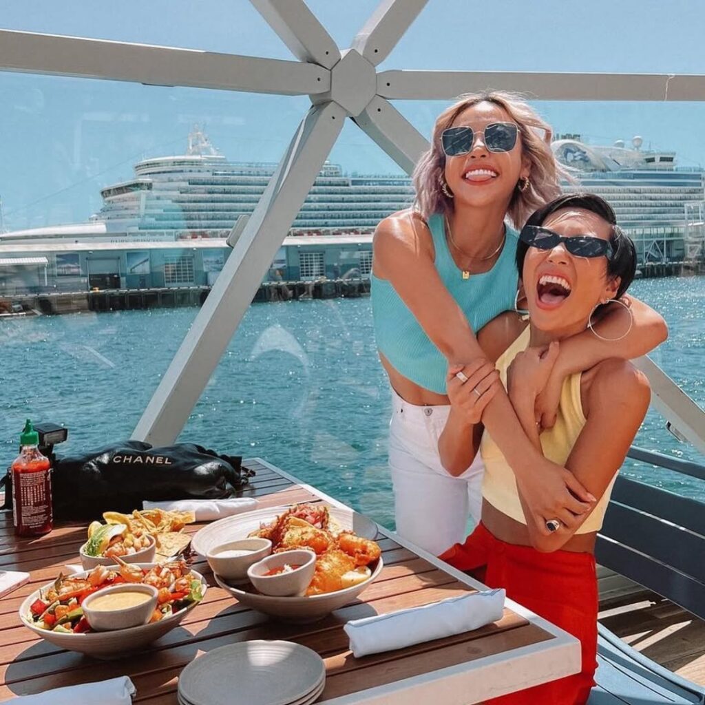 Two girls standing by table, with water in the background